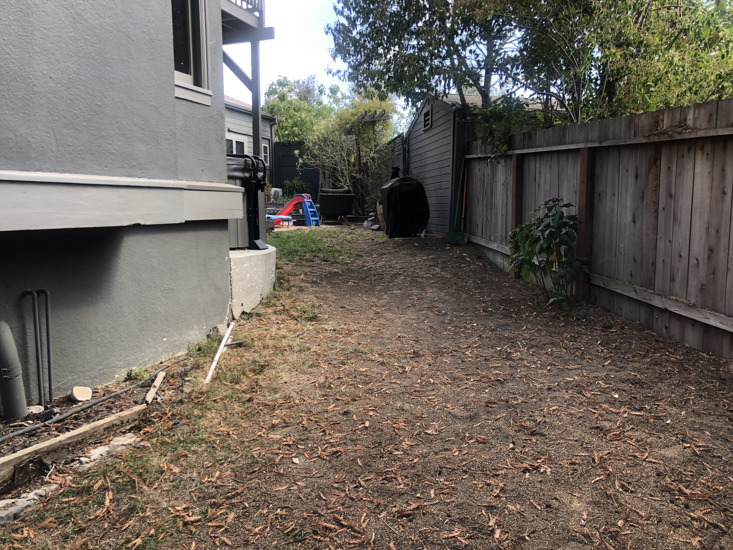 Side yard before — bare dirt path between house and fence